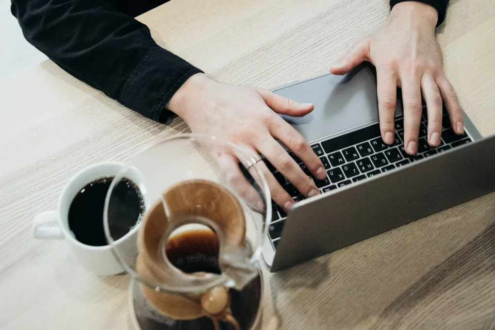 Person typing on a laptop next to a cup of coffee